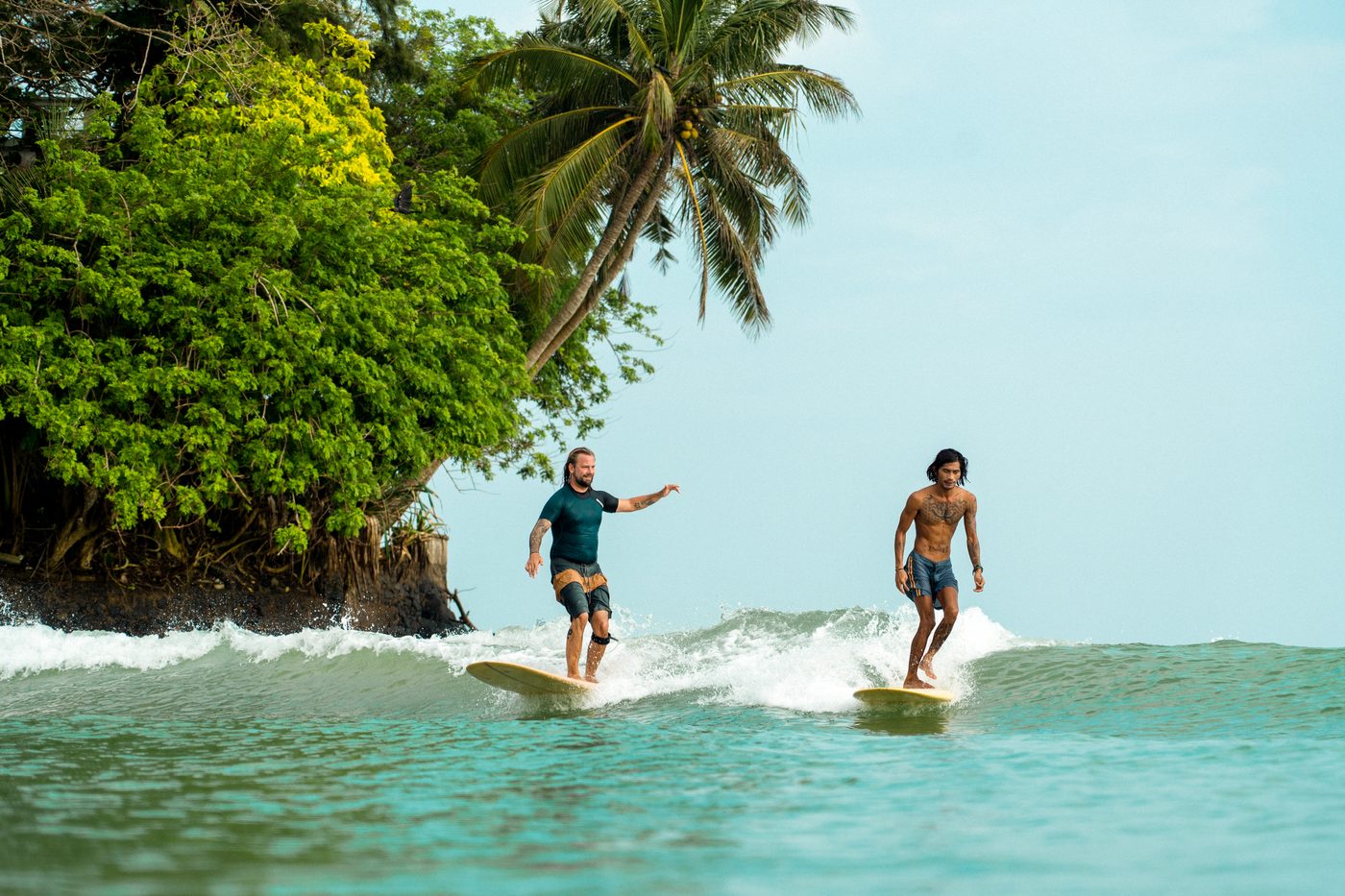 Two surfers riding the same wave past a rocky point in Sri Lanka
